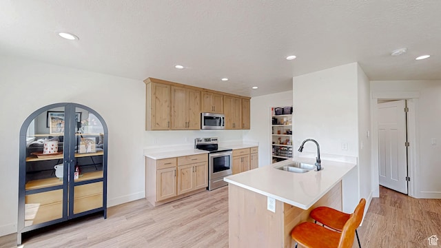 628 E 625 S, Nephi, UT 84648 - kitchen with appliances with stainless steel finishes, light wood finished floors, a kitchen bar, light brown cabinetry, and a peninsula