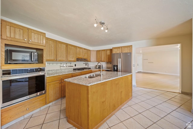 8463 S Jackson Hole Dr E, Sandy, UT 84093 - kitchen featuring appliances with stainless steel finishes, light tile patterned flooring, a kitchen island with sink, and light stone counters