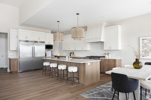 14277 S Keely Ct, Bluffdale, UT 84065 - kitchen with built in appliances, custom exhaust hood, wood finished floors, a kitchen breakfast bar, and backsplash