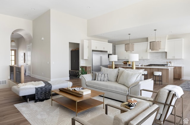 14277 S Keely Ct, Bluffdale, UT 84065 - living room featuring arched walkways, light wood-style flooring, a towering ceiling, and recessed lighting