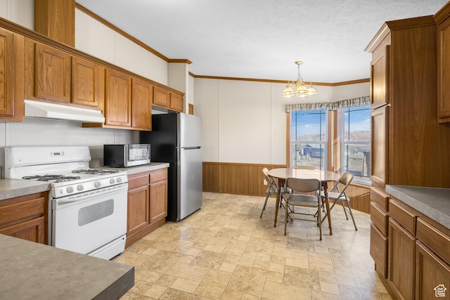 2627 E Cactus Rd, Moab, UT 84532 - kitchen featuring appliances with stainless steel finishes, under cabinet range hood, crown molding, brown cabinetry, and a chandelier
