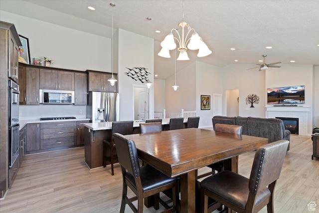 1381 W 425 S, Layton, UT 84041 - dining space with high vaulted ceiling, a chandelier, light wood-style flooring, a glass covered fireplace, and ceiling fan