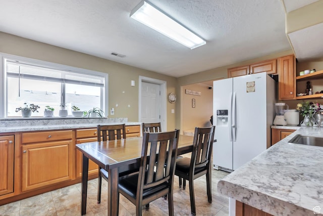 6088 W Graceland Way, West Jordan, UT 84081 - kitchen featuring white fridge with ice dispenser, light countertops, open shelves, brown cabinetry, and a textured ceiling