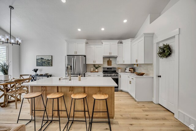 468 W Sunnyrise Ln S, Stansbury Park, UT 84074 - kitchen with appliances with stainless steel finishes, decorative backsplash, a breakfast bar, a center island with sink, and light wood finished floors