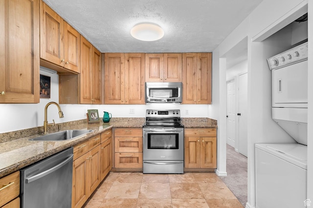 314 W Center St Unit 123, Bountiful, UT 84010 - kitchen featuring appliances with stainless steel finishes, stacked washer / dryer, stone countertops, a textured ceiling, and brown cabinetry