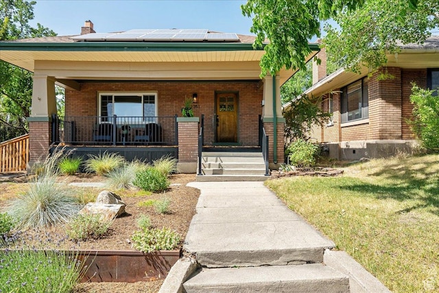 1351 E Browning Ave S, Salt Lake City, UT 84105 - view of front of house featuring covered porch, brick siding, roof mounted solar panels, a chimney, and a front lawn