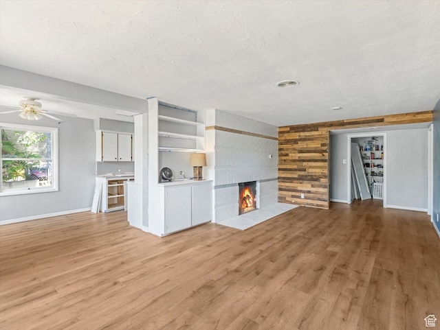 1815 E Hillcrest Ave, Salt Lake City, UT 84106 - unfurnished living room featuring light wood finished floors, wood walls, a tiled fireplace, a ceiling fan, and a textured ceiling