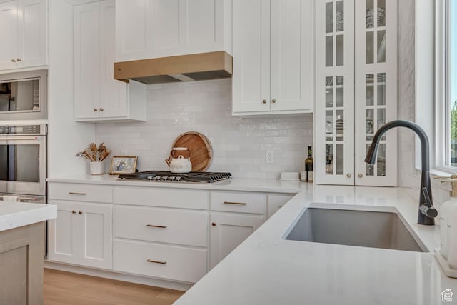 10948 S Samoa Dune Dr Unit 1027, South Jordan, UT 84009 - kitchen featuring stainless steel appliances, wall chimney exhaust hood, white cabinetry, backsplash, and glass insert cabinets