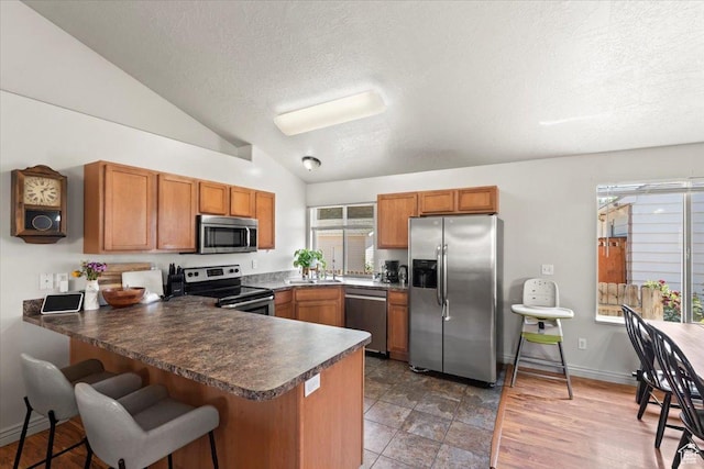 1544 Liberty Ave, Ogden, UT 84404 - kitchen with stainless steel appliances, a peninsula, brown cabinetry, lofted ceiling, and dark countertops