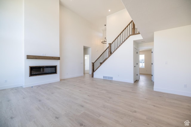361 E Ventura Blvd, Tooele, UT 84074 - unfurnished living room featuring stairs, light wood-type flooring, a towering ceiling, a glass covered fireplace, and recessed lighting