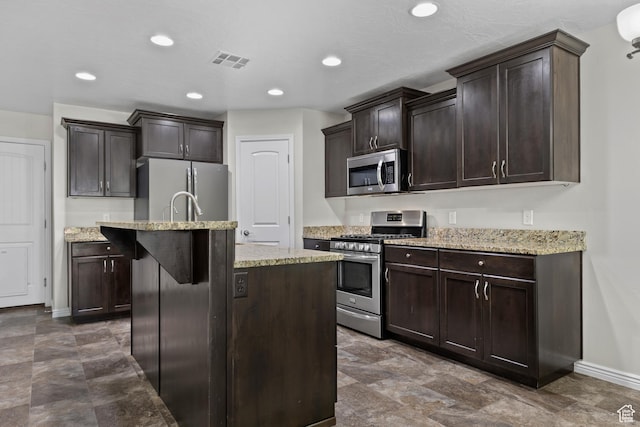 3342 S 240 W, Washington, UT 84780 - kitchen featuring appliances with stainless steel finishes, dark brown cabinetry, a center island with sink, light stone counters, and recessed lighting