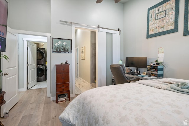 6447 W Arranmore Dr, South Jordan, UT 84009 - bedroom featuring stacked washer / dryer, a barn door, light wood-type flooring, and a high ceiling