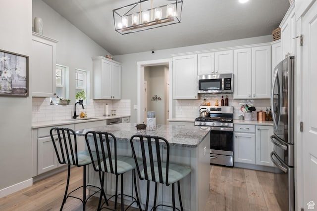 6447 W Arranmore Dr, South Jordan, UT 84009 - kitchen with appliances with stainless steel finishes, a center island, backsplash, light wood-style flooring, and light stone counters