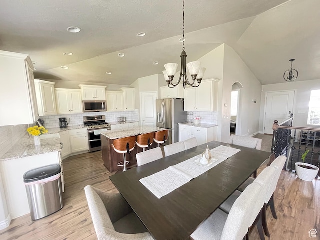 2433 N 1445 W, Clinton, UT 84015 - dining room featuring vaulted ceiling, a chandelier, arched walkways, and light wood-style flooring