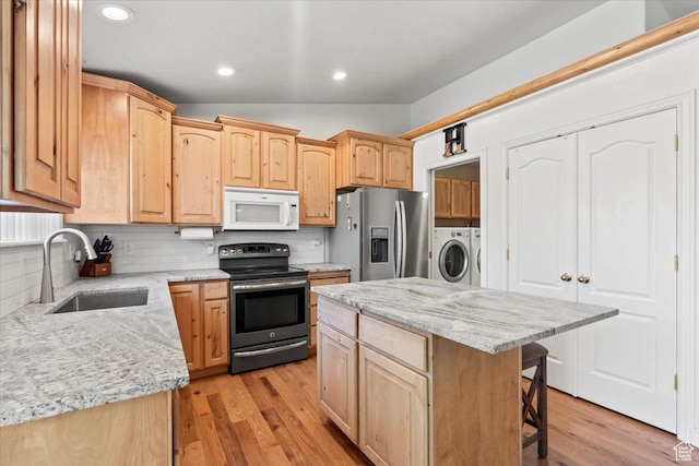 7217 W Mccuiston Ave S, Herriman, UT 84096 - kitchen with stainless steel appliances, washing machine and dryer, light brown cabinetry, a breakfast bar area, and vaulted ceiling