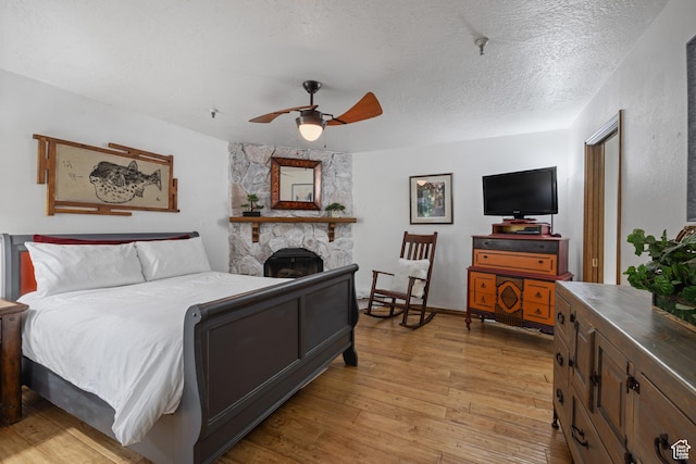 1035 Park Ave Unit 7-G, Park City, UT 84060 - bedroom with light wood-style flooring, a textured ceiling, a stone fireplace, and a ceiling fan