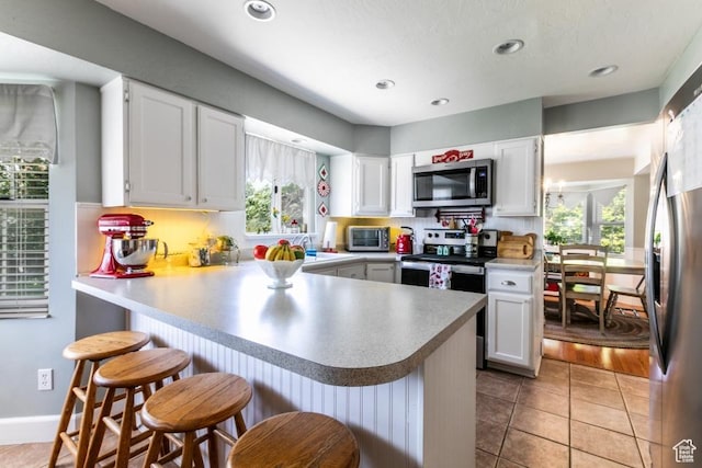 5668 S 1090 W, Murray, UT 84123 - kitchen with appliances with stainless steel finishes, a peninsula, white cabinets, a breakfast bar, and healthy amount of natural light