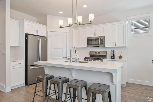 1304 E Weyburn Ln S Unit 10, Holladay, UT 84117 - kitchen featuring appliances with stainless steel finishes, white cabinetry, a kitchen breakfast bar, light wood-style flooring, and an island with sink