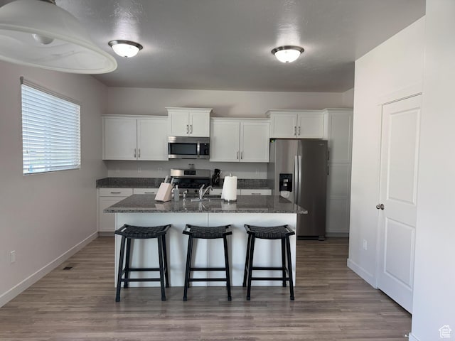 1637 S 730 W, Provo, UT 84601 - kitchen featuring appliances with stainless steel finishes, a kitchen bar, white cabinetry, a kitchen island with sink, and wood finished floors