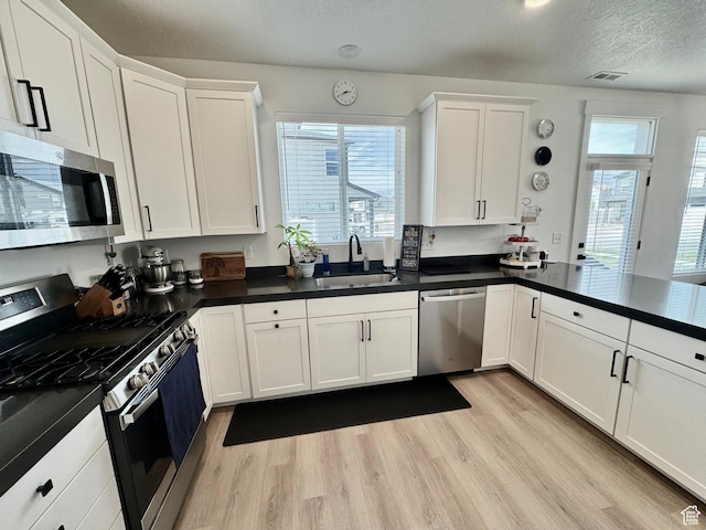 1038 W 980 S Unit 312, American Fork, UT 84003 - kitchen with appliances with stainless steel finishes, light wood finished floors, white cabinets, dark countertops, and a textured ceiling