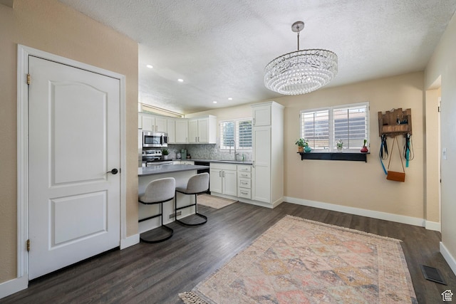 6764 S Enchanted Dr E, Midvale, UT 84047 - kitchen featuring appliances with stainless steel finishes, a textured ceiling, white cabinetry, dark wood-style floors, and backsplash