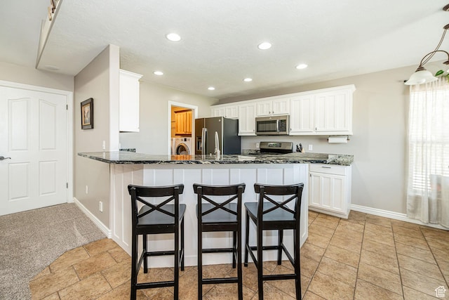 3520 W 2600 N, Plain City, UT 84404 - kitchen featuring stainless steel appliances, a breakfast bar area, washer / dryer, white cabinetry, and dark stone counters