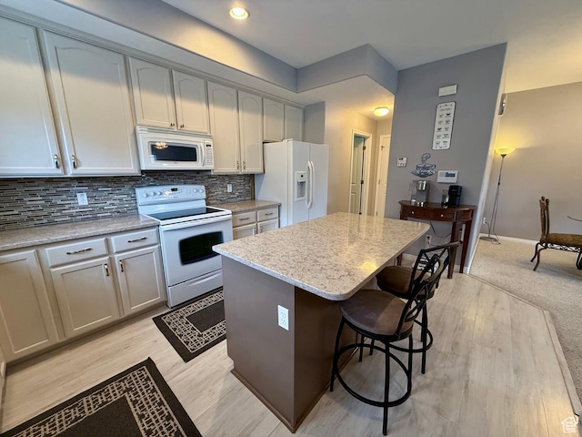7089 S Brittany Town Dr, West Jordan, UT 84084 - kitchen featuring white appliances, a kitchen island, a breakfast bar, decorative backsplash, and light stone countertops
