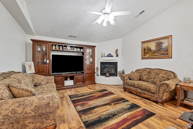 3430 Red Butte Dr, Santa Clara, UT 84765 - living room featuring light wood finished floors, a ceiling fan, a glass covered fireplace, and a textured ceiling