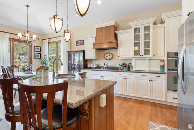 14599 S Chaumont Ct, Draper, UT 84020 - kitchen featuring custom range hood, stainless steel appliances, a breakfast bar area, light stone counters, and a chandelier
