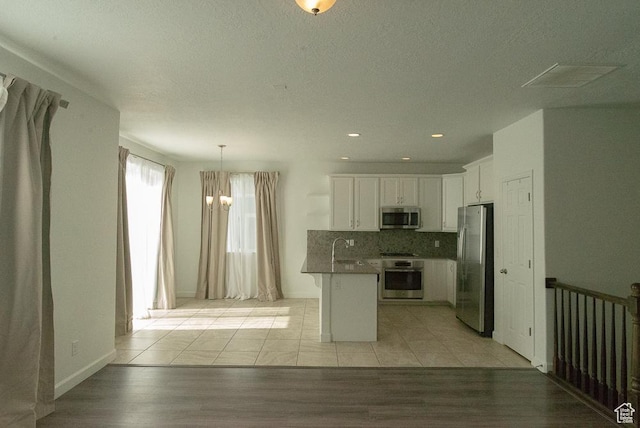 63 N Canyon Maple Rd, Vineyard, UT 84059 - kitchen with appliances with stainless steel finishes, a peninsula, white cabinets, backsplash, and hanging light fixtures
