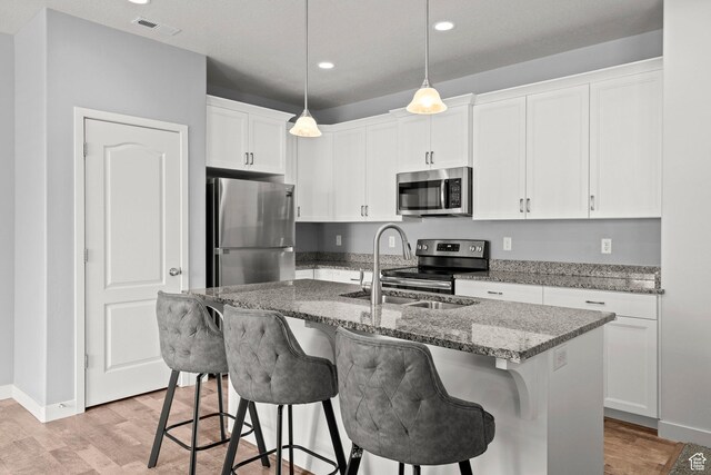 5423 W Black Hills Ln, Herriman, UT 84096 - kitchen featuring appliances with stainless steel finishes, light wood-style floors, a breakfast bar, stone counters, and white cabinetry