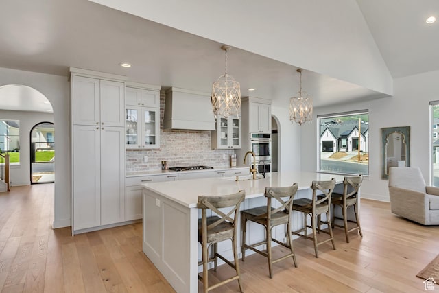481 E 3675 N, North Ogden, UT 84414 - kitchen featuring arched walkways, custom exhaust hood, appliances with stainless steel finishes, light wood-style floors, and a center island with sink