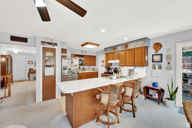11901 S Maple Ridge Rd, Sandy, UT 84094 - kitchen featuring light colored carpet, brown cabinetry, stainless steel appliances, a peninsula, and light countertops