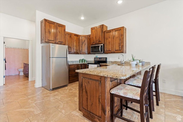 1145 W 500 N, Manti, UT 84642 - kitchen featuring appliances with stainless steel finishes, a peninsula, light stone countertops, a breakfast bar, and brown cabinetry
