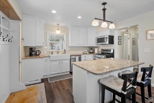 5203 Chambers St, South Ogden, UT 84403 - kitchen with stainless steel appliances, dark wood-type flooring, white cabinetry, a breakfast bar area, and decorative light fixtures