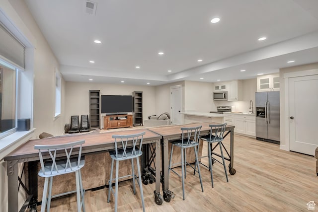 2040 E Lambourne Ave, Millcreek, UT 84109 - kitchen featuring appliances with stainless steel finishes, white cabinets, light wood-type flooring, a kitchen bar, and glass insert cabinets