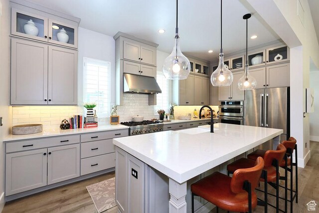 7817 S Danish Pine Ln Unit 101, Cottonwood Heights, UT 84121 - kitchen with under cabinet range hood, wood finished floors, a center island with sink, decorative backsplash, and a breakfast bar