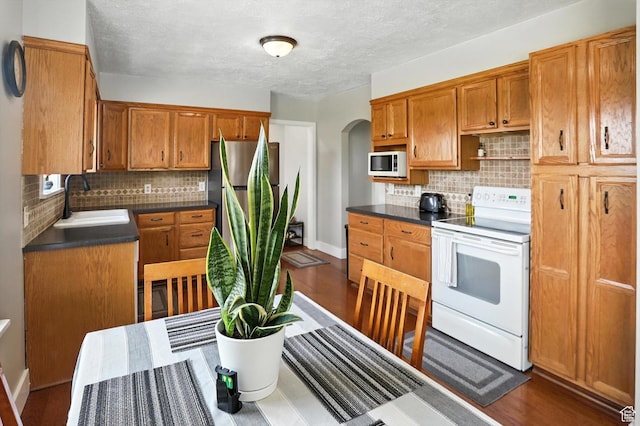 11395 N 4400 W, Tremonton, UT 84337 - kitchen featuring white appliances, arched walkways, tasteful backsplash, dark countertops, and brown cabinets