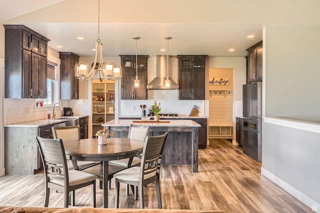 4909 N Cliffrose Dr, Eagle Mountain, UT 84005 - kitchen featuring wall chimney range hood, a kitchen island, light wood-type flooring, a chandelier, and dark brown cabinetry