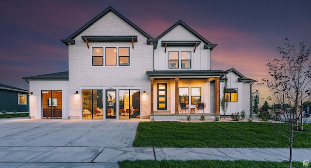 4625 N Fallow Way Unit 513, Eagle Mountain, UT 84005 - back of house at dusk with board and batten siding, a porch, a yard, and brick siding