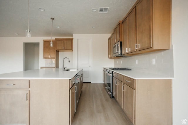 43 Rosalia Rdg, St George, UT 84770 - kitchen featuring appliances with stainless steel finishes, light wood finished floors, decorative backsplash, brown cabinets, and a center island with sink