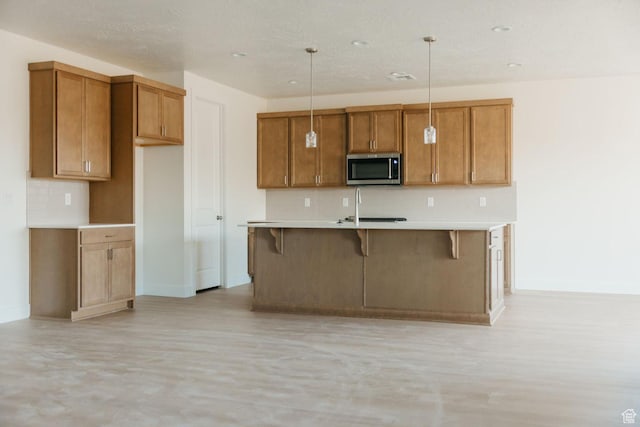 43 Rosalia Rdg, St George, UT 84770 - kitchen featuring stainless steel microwave, tasteful backsplash, brown cabinets, and an island with sink