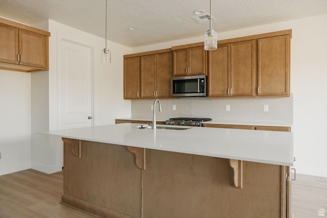 43 Rosalia Rdg, St George, UT 84770 - kitchen featuring stainless steel microwave, light wood finished floors, brown cabinetry, hanging light fixtures, and light countertops