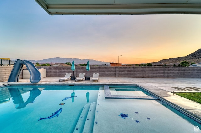 3410 W 2490 S, Hurricane, UT 84737 - pool at dusk featuring a mountain view, a water slide, a patio, and a pool with connected hot tub