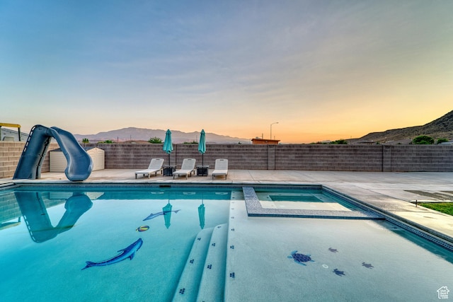 3410 W 2490 S, Hurricane, UT 84737 - pool at dusk featuring a water slide, a mountain view, a patio, and a pool with connected hot tub