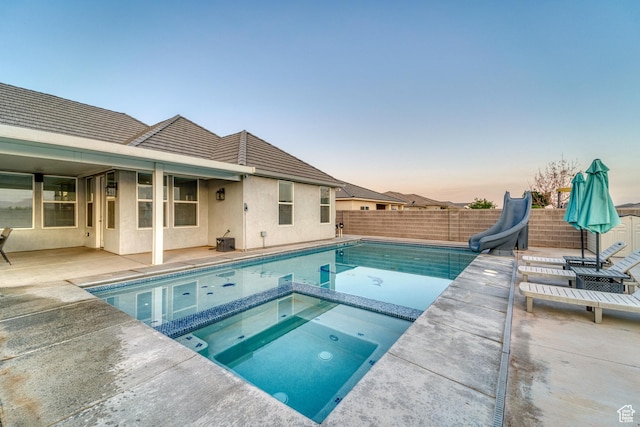 3410 W 2490 S, Hurricane, UT 84737 - pool at dusk featuring a water slide, a patio area, a fenced backyard, and a pool with connected hot tub