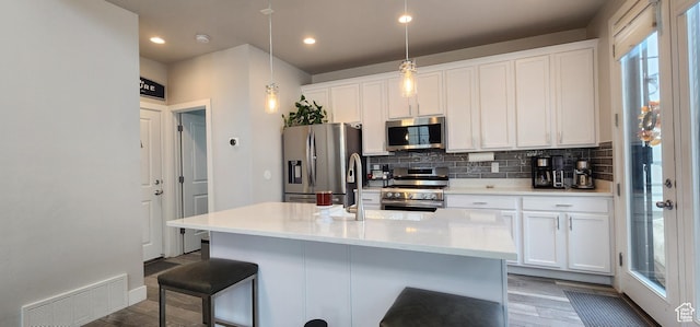 5332 W Scout Plane Ln, South Jordan, UT 84009 - kitchen featuring appliances with stainless steel finishes, wood finished floors, white cabinets, decorative backsplash, and a kitchen breakfast bar