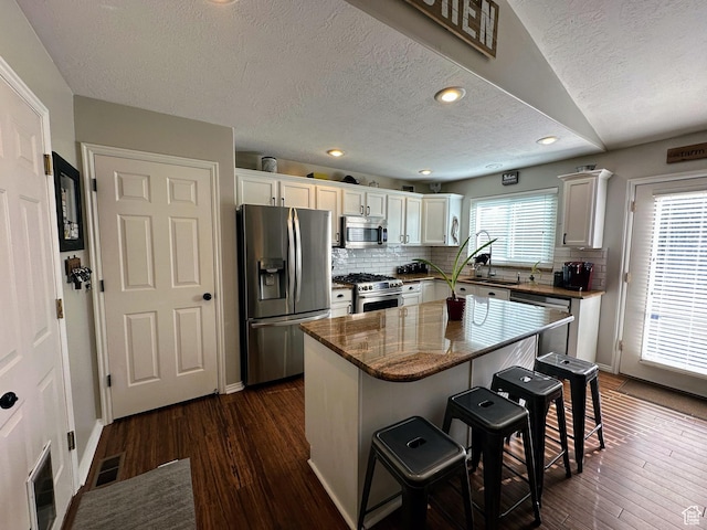 8675 S Pebblecreek Rd, West Jordan, UT 84081 - kitchen with stainless steel appliances, a textured ceiling, a breakfast bar area, white cabinetry, and tasteful backsplash