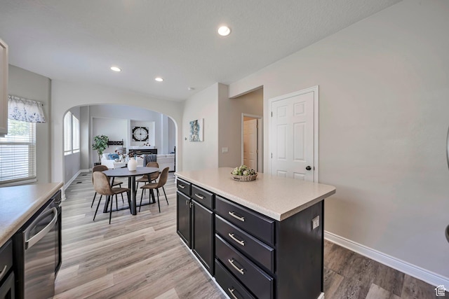 5961 W Chiswick Ct, West Jordan, UT 84081 - kitchen featuring arched walkways, stainless steel dishwasher, dark cabinetry, light countertops, and a center island