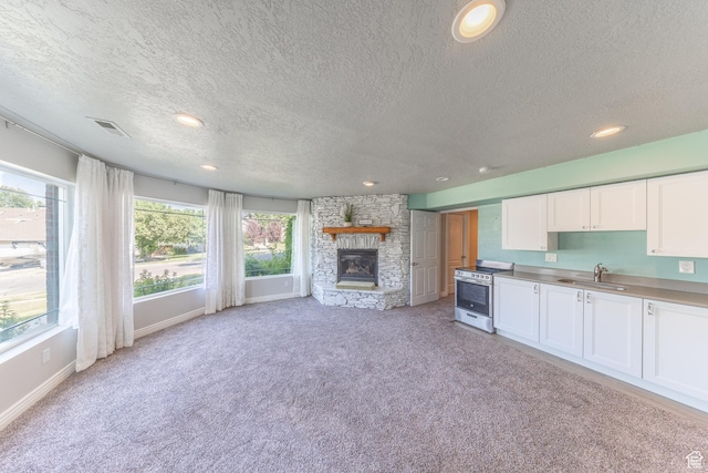 1320 E Canberra Dr, Lindon, UT 84042 - kitchen with stainless steel electric stove, a textured ceiling, light carpet, white cabinets, and a fireplace